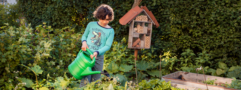 Barn i pyjamas som vattnar plantering med  vattenkanna