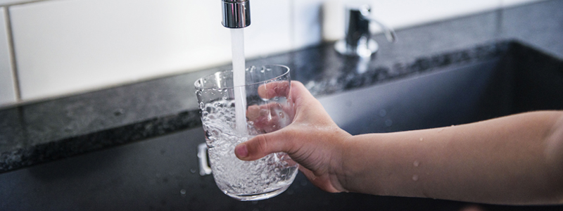 Hand håller i glas som fylls med vatten från kranen